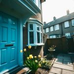 A pastel blue composite front door with symmetrical panels and chrome fixtures on a modern British home, framed by blooming spring flowers. This image showcases Vista Panels' stylish and durable composite doors, ideal for enhancing a home’s entrance.